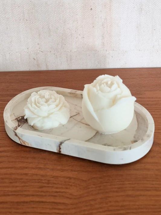 Eine Rosen- und eine Pfingstrosenkerze in naturweiss auf einem Kerzenteller