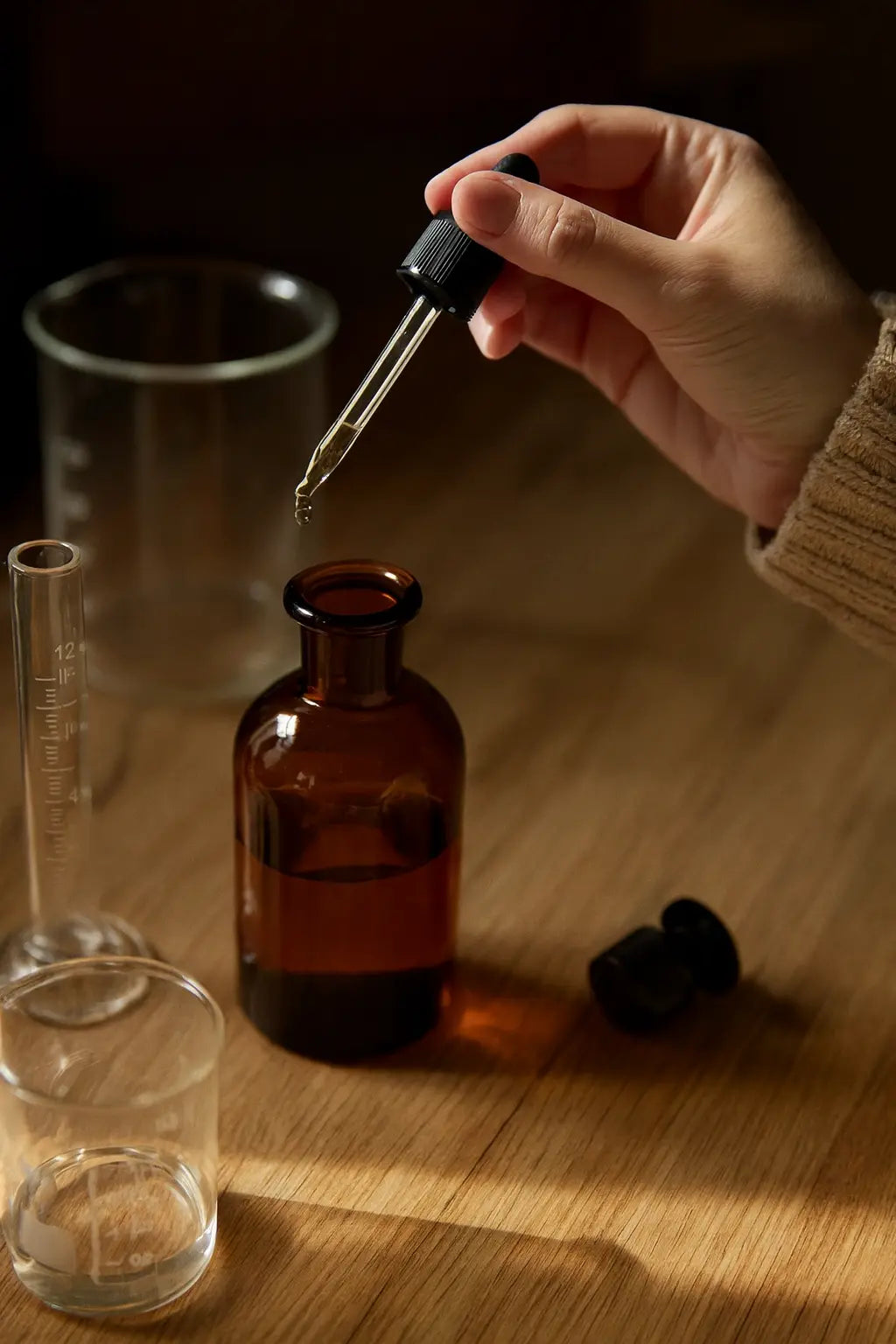 Unterschiedliche Flaschen und Gefässe auf einem Holztisch. Eine Hand träufelt ätherisches Öl mit einer Pipette in ein Gefäss.