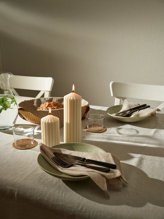 Zwei Zylinderkerzen mit grossen Rillen auf einem gedeckten Tisch.