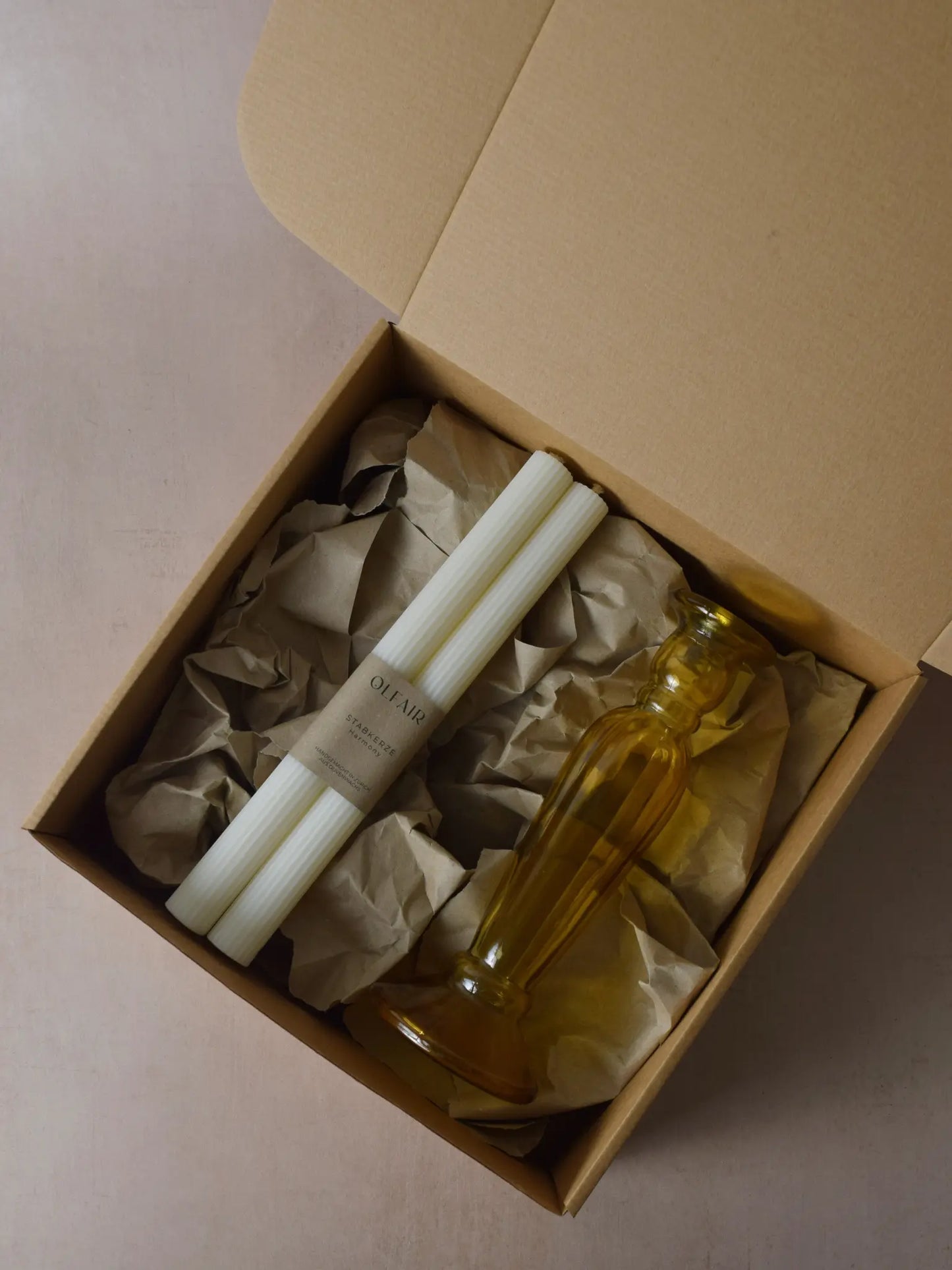 Geschenkset bestehend aus einem 2er-Set Stabkerzen mit kleinen Rilen und einem bernsteinfarbenen Kerzenhalter aus Recycling-Glas