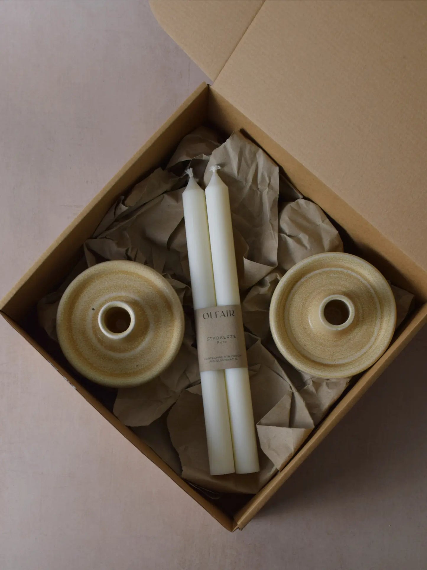 Geschenkset bestehend aus einem 2er-Set glatten Stabkerzen und zwei Kerzenhaltern aus Keramik in beige.