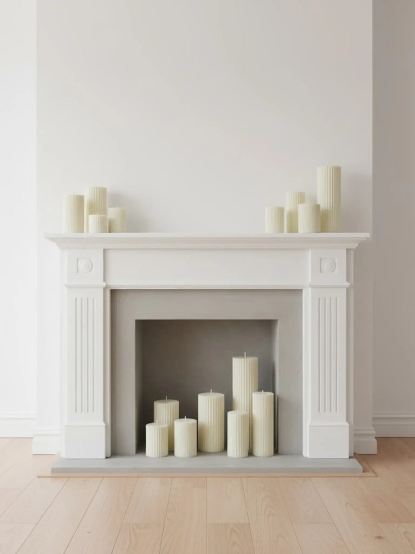 Unterschiedliche grosse Zylinderkerzen mit feinen Rillen in und auf einem weissen Kamin.