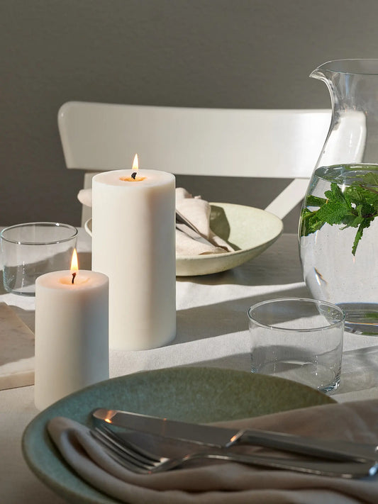 Zwei unterschiedlich grosse Zylinderkerzen auf einem gedeckten Tisch