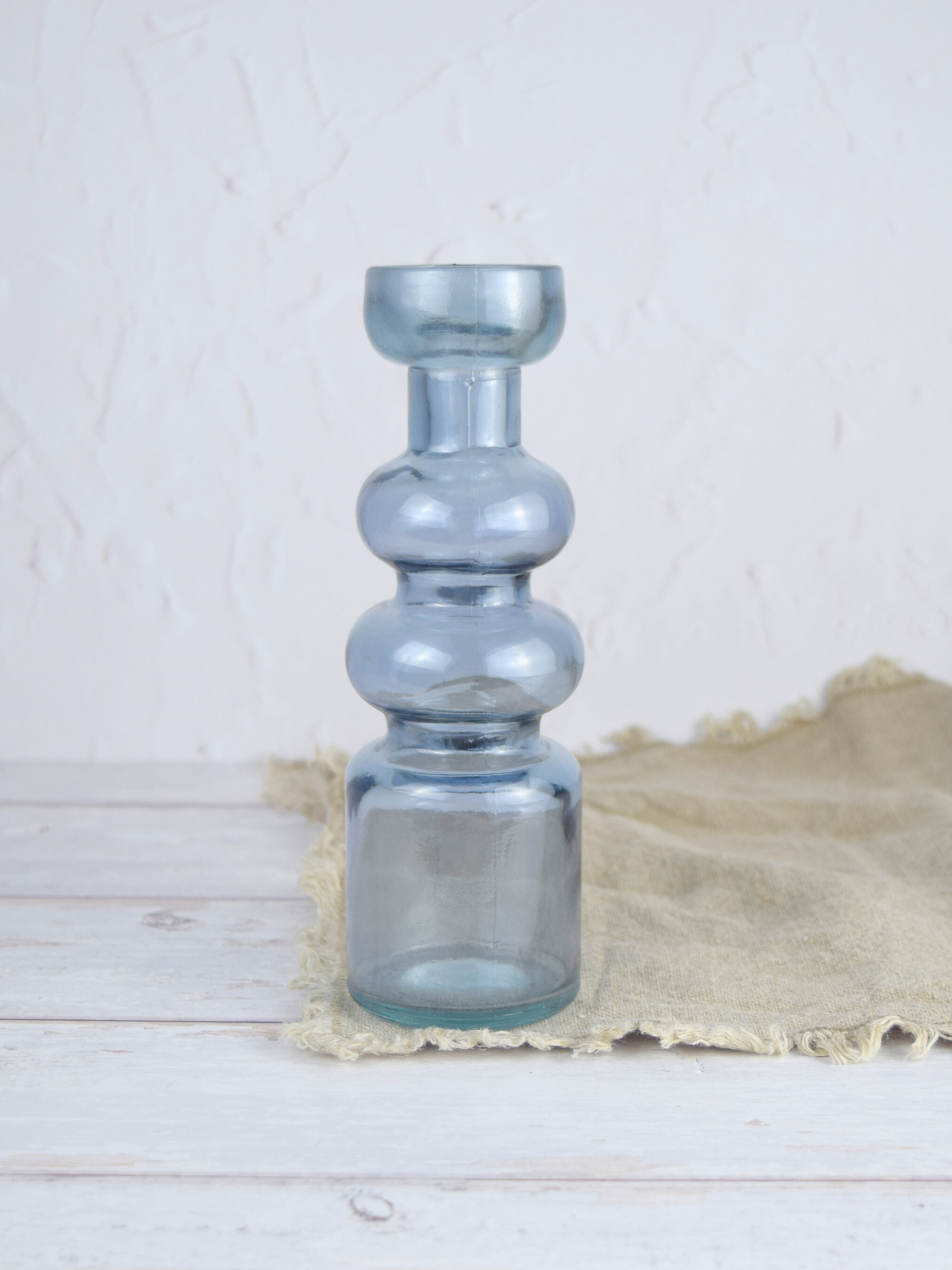 Blauer, gewölbter Kerzenhalter auf einem braunen Tuch vor einem weissen Hintergrund
