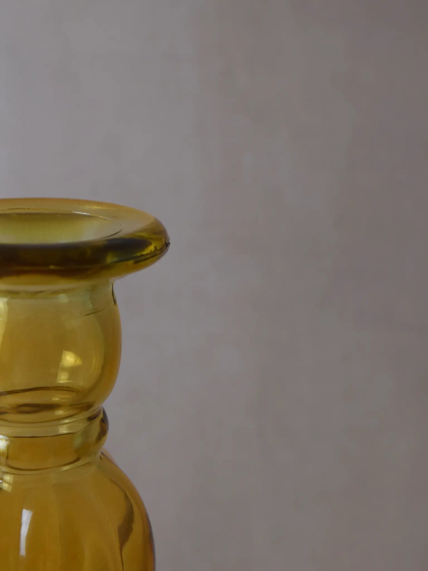 Teilaufnahme eines senfarbigen Kerzenhalters aus Recyclingglas auf einem beigen Hintergrund.