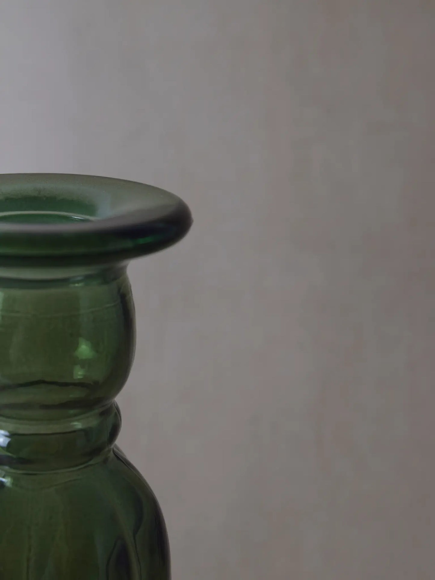 Teilaufnahme eines grünen Kerzenhalters aus Recyclingglas auf einem beigen Hintergrund.