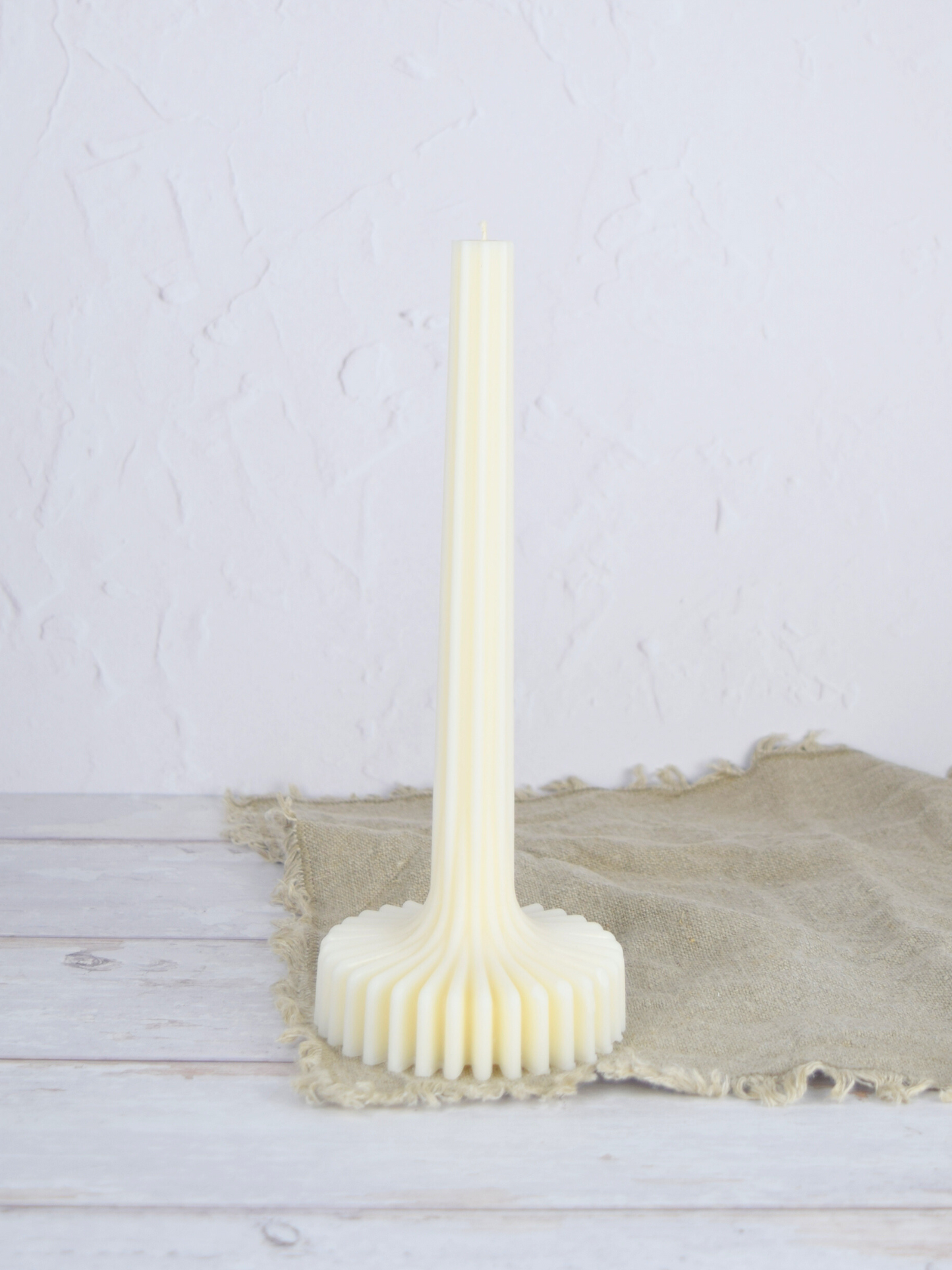 Naturweisse Stabkerze mit Sockel auf einem braunen Tuch vor einem weiss Hintergrund