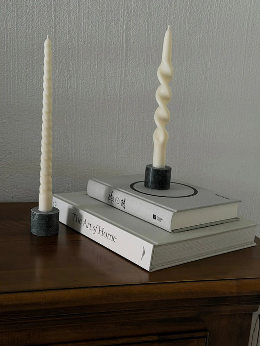 Zwei verschieden gedrehte Stabkerzen auf einer Holzkommode. Einer Stabkerze steht auf zwei Büchern.