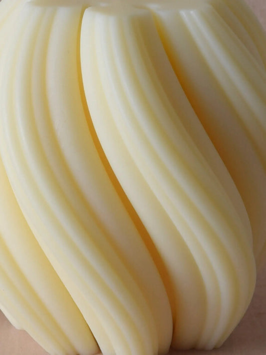 Nahaufnahme einer Kerze mit spiralförmiger Struktur vor einem beigen Hintergrund.