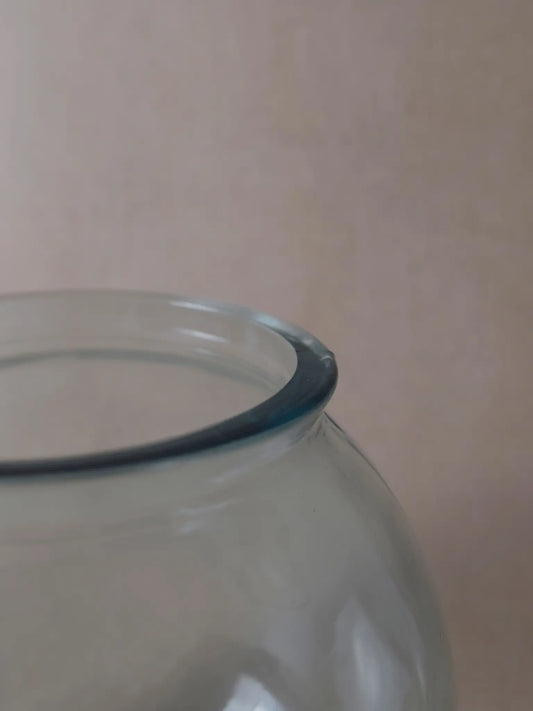 Nahaufnahme einer durchsichtigen, runden Vase vor einem beigen Hintergrund