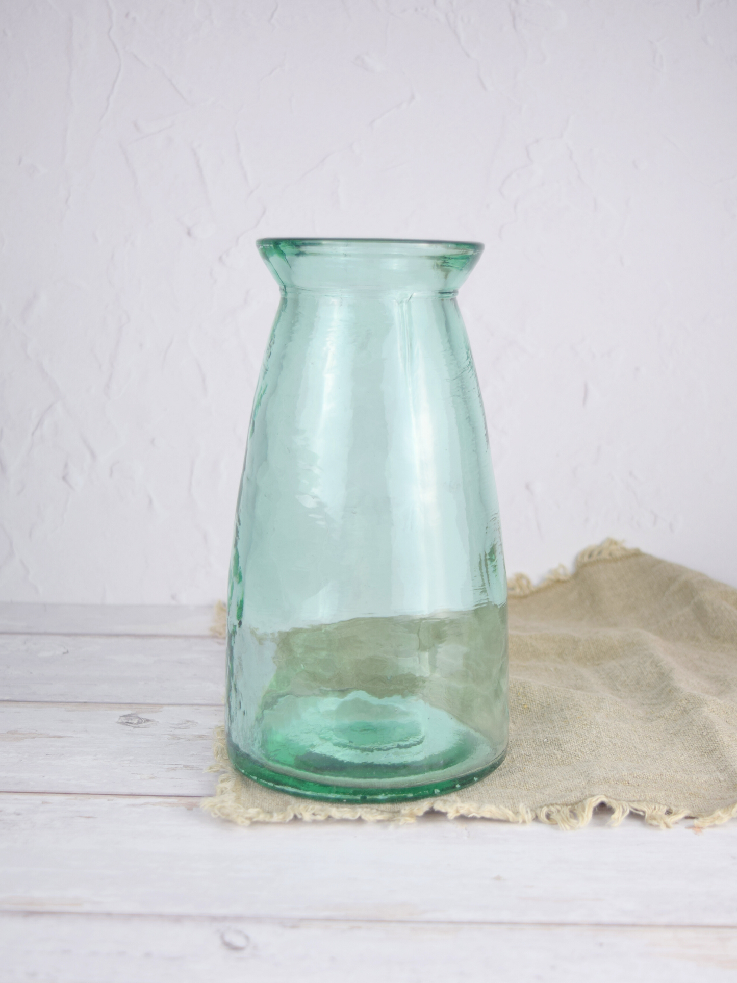 Bläuliche, grosse Vase auf einem braunen Tuch vor einem weissen Hintergrund