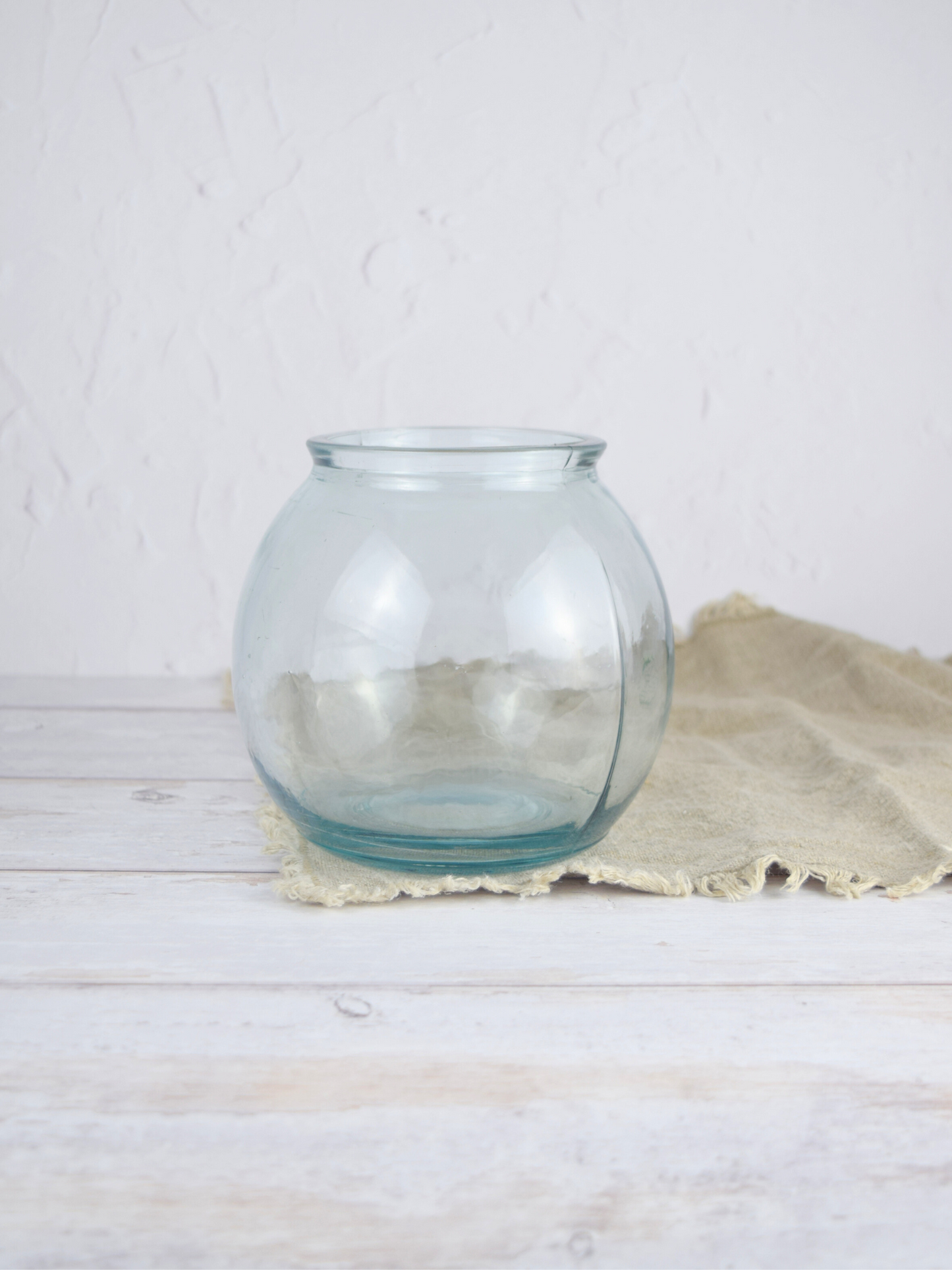 Durchsichtige, runde Vase auf einem braunen Tuch vor einem weissen Hintergrund