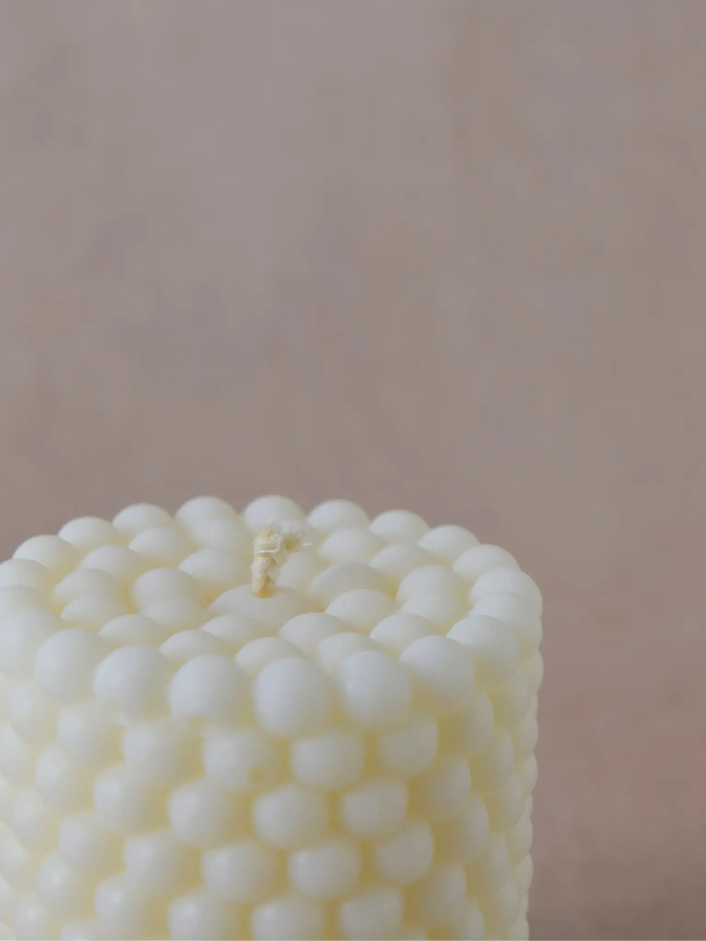 Nahaufnahme einer Zylinderkerze in Bubble-Struktur in naturweiss auf einem beigen Hintergrund