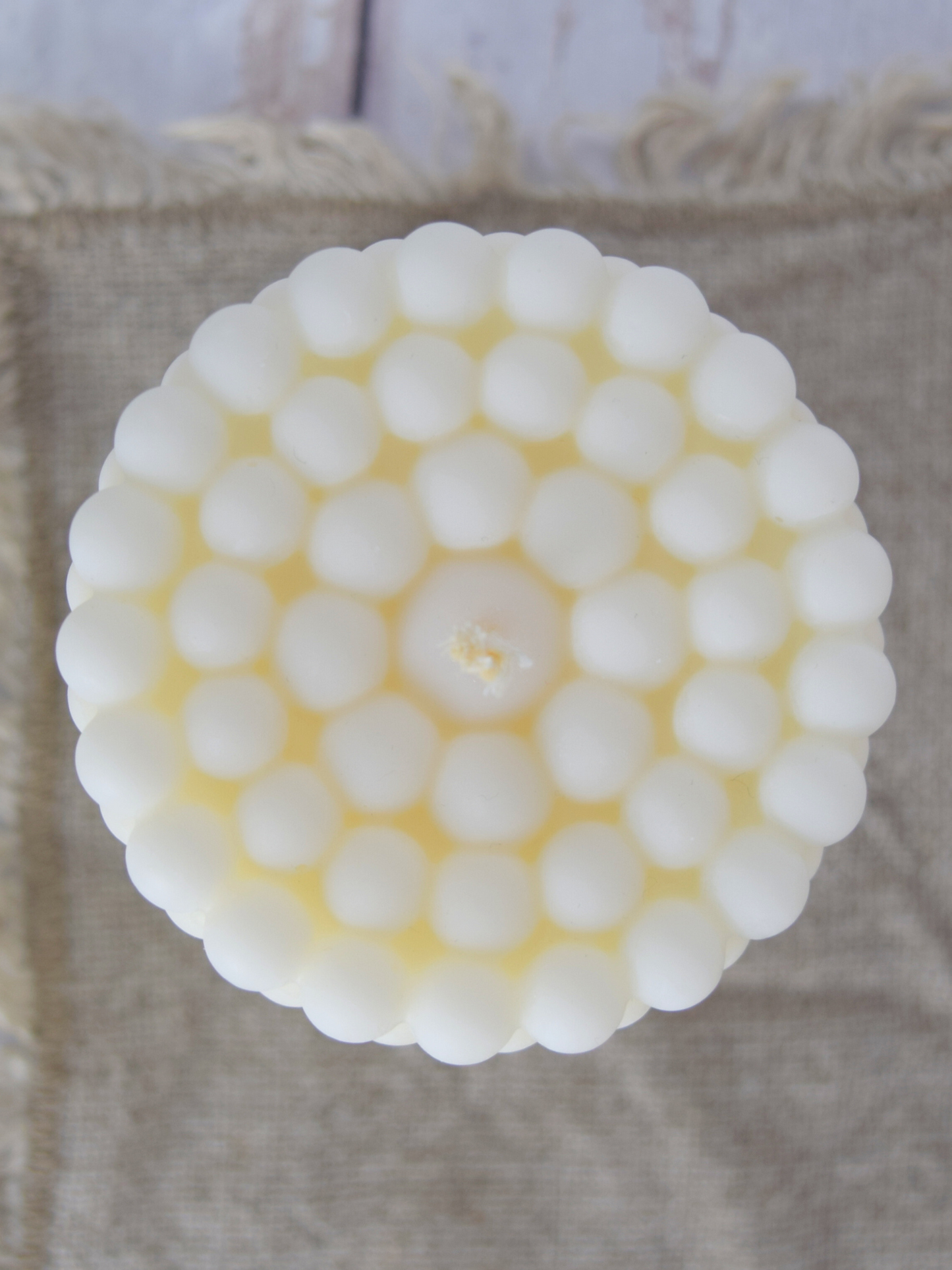 Nahaufnahme einer Zylinderkerze mit Bubble-Struktur in naturweiss auf einem braunen Tuch.