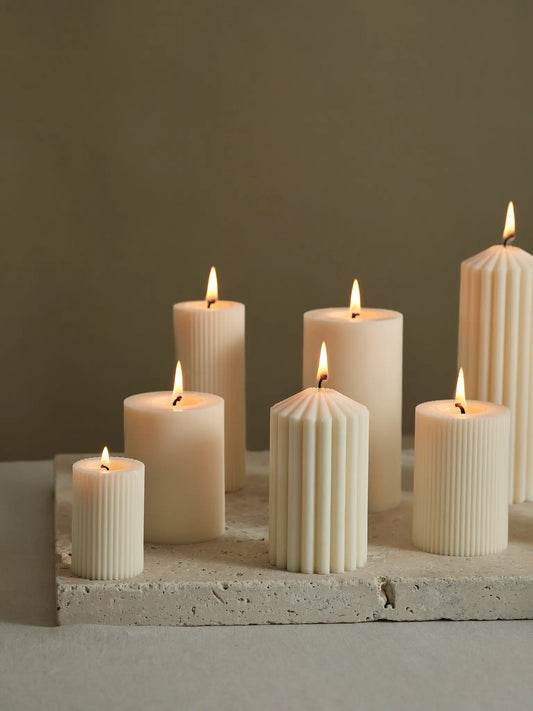 Unterschiedlich grosse Zylinderkerzen mit Rillenstruktur auf einem Naturstein.