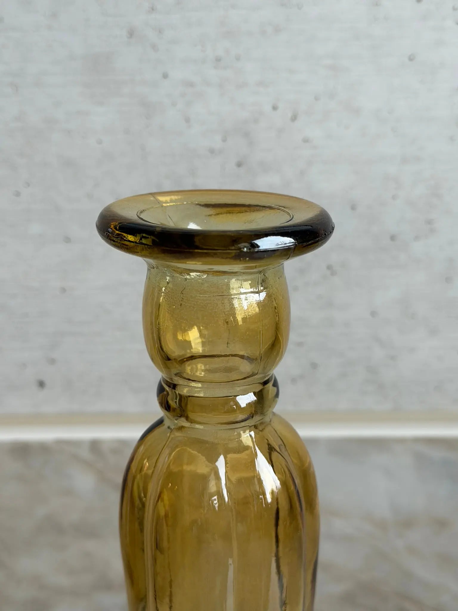 Nahaufnahme eines senfarbigen Kerzenhalters aus Recyclingglas auf einem Marmor Hintergrund.