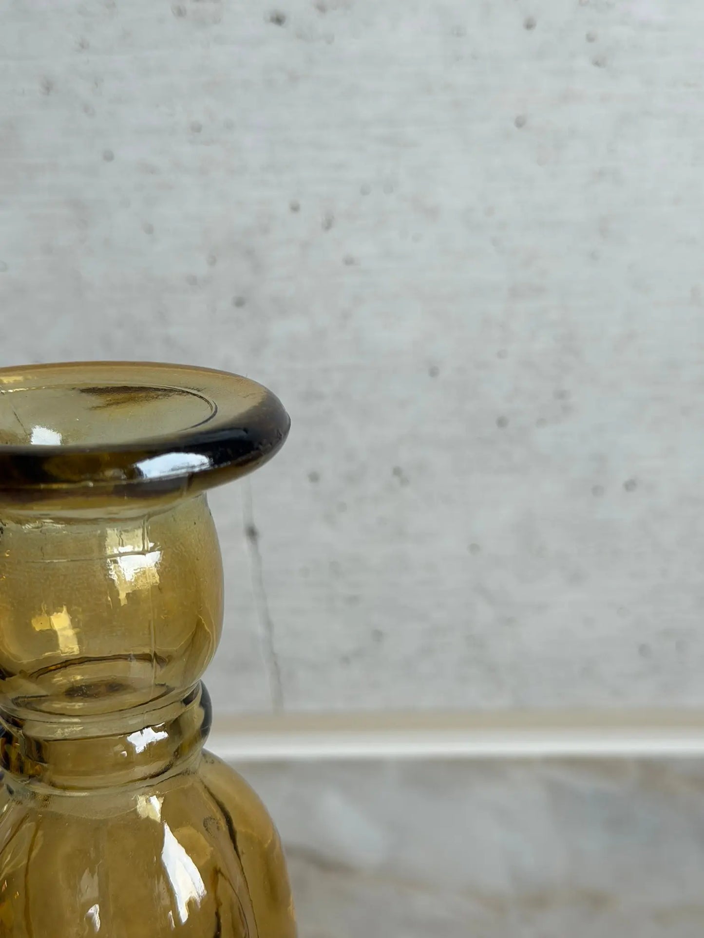 Teilaufnahme eines senfarbigen Kerzenhalters aus Recyclingglas auf einem Marmor Hintergrund.