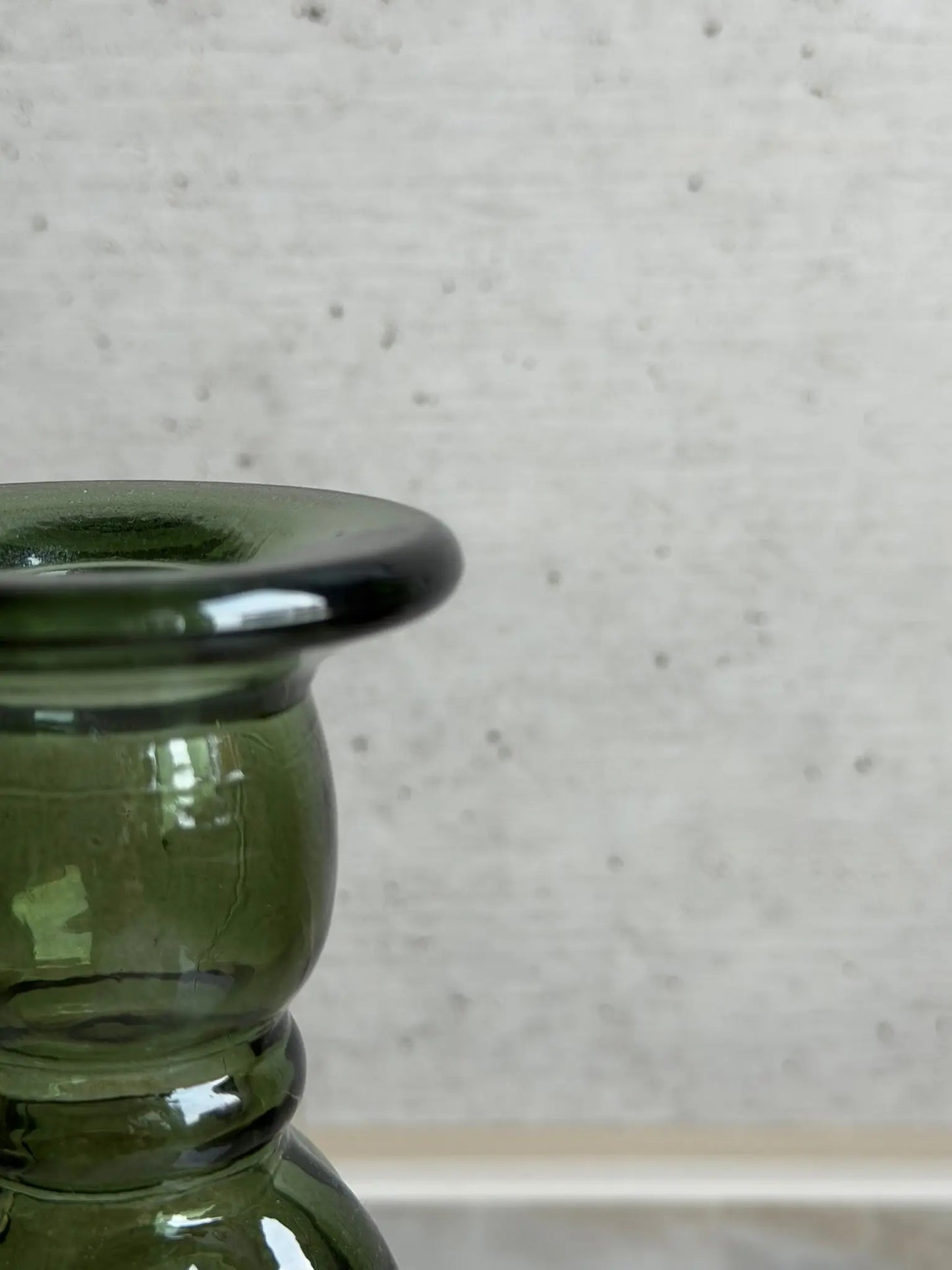 Teilaufnahme eines grünen Kerzenhalters aus Recyclingglas auf einem Marmor Hintergrund.