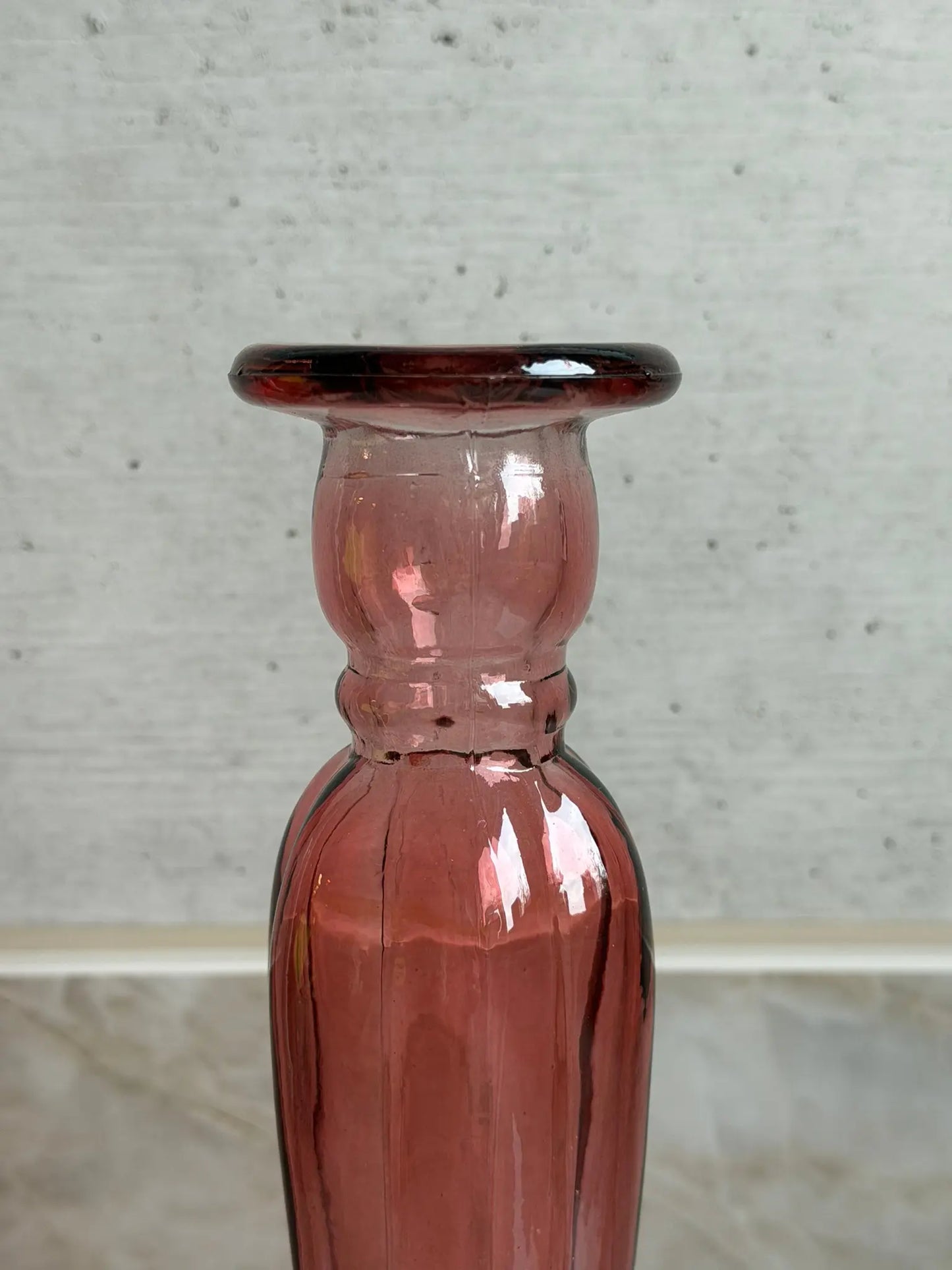 Nahaufnahme eines rosafarbigen Kerzenhalters aus Recyclingglas auf einem Marmor Hintergrund.