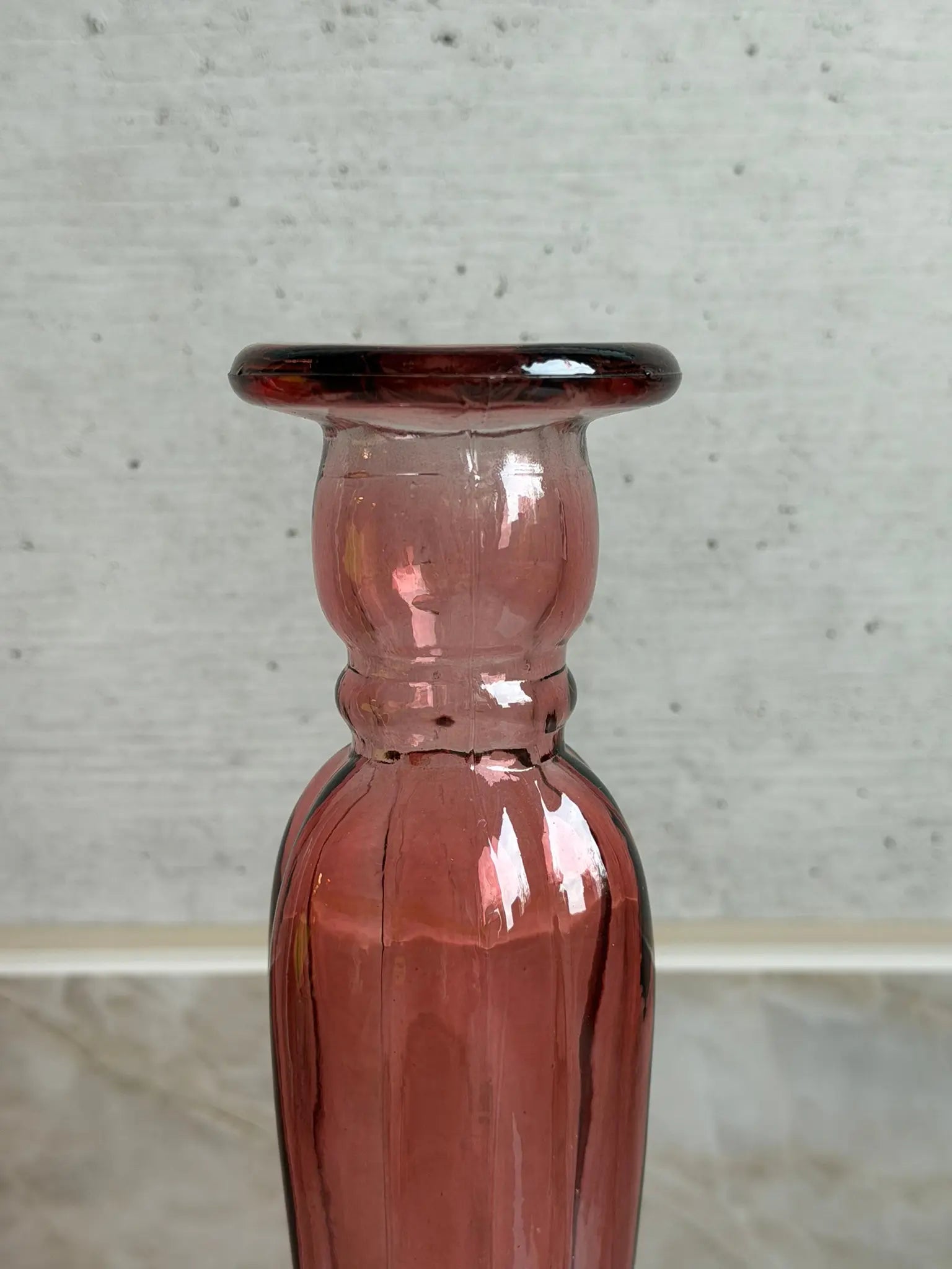 Nahaufnahme eines rosafarbigen Kerzenhalters aus Recyclingglas auf einem Marmor Hintergrund.