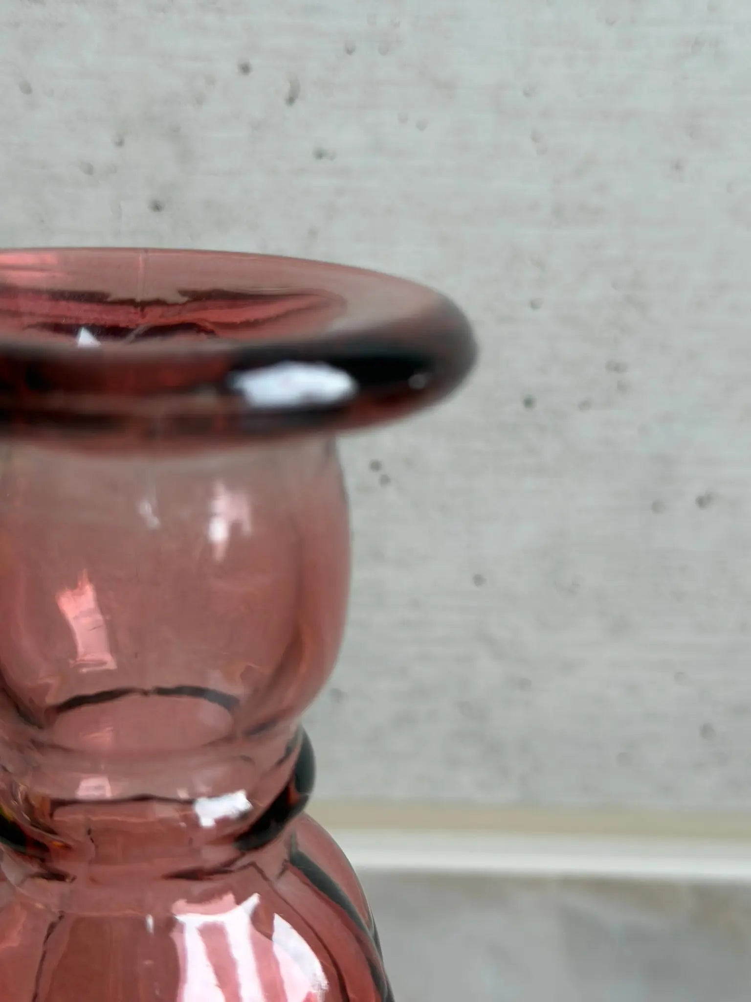 Teilaufnahme eines rosaarbigen Kerzenhalters aus Recyclingglas auf einem Marmor Hintergrund.
