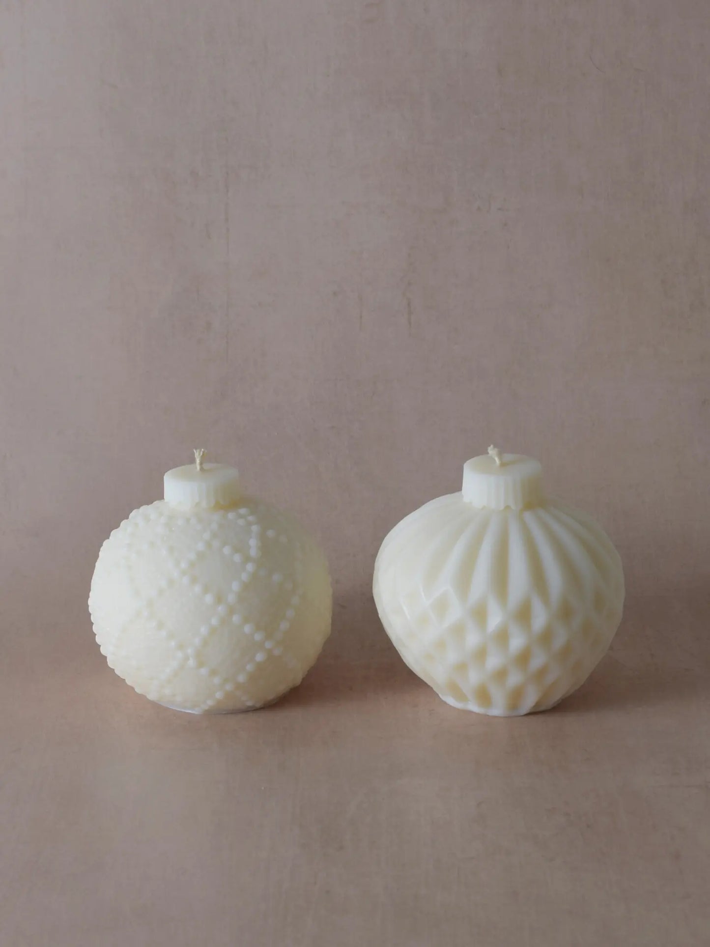 Zwei naturfarbene Kerzen in Weihnachtskugelform mit kleinen Tupfen und Streifen.