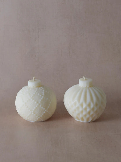 Zwei naturfarbene Kerzen in Weihnachtskugelform mit kleinen Tupfen und Streifen.