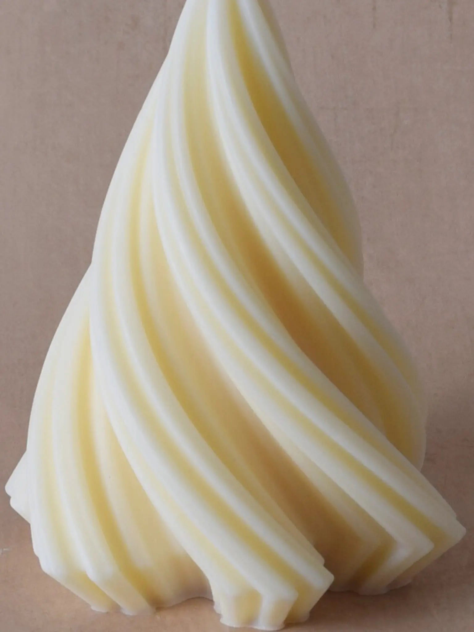 Nahaufname einer naturfarbenen Kerze in Weihnachtsbaumform vor einem beigen Hintergrund.