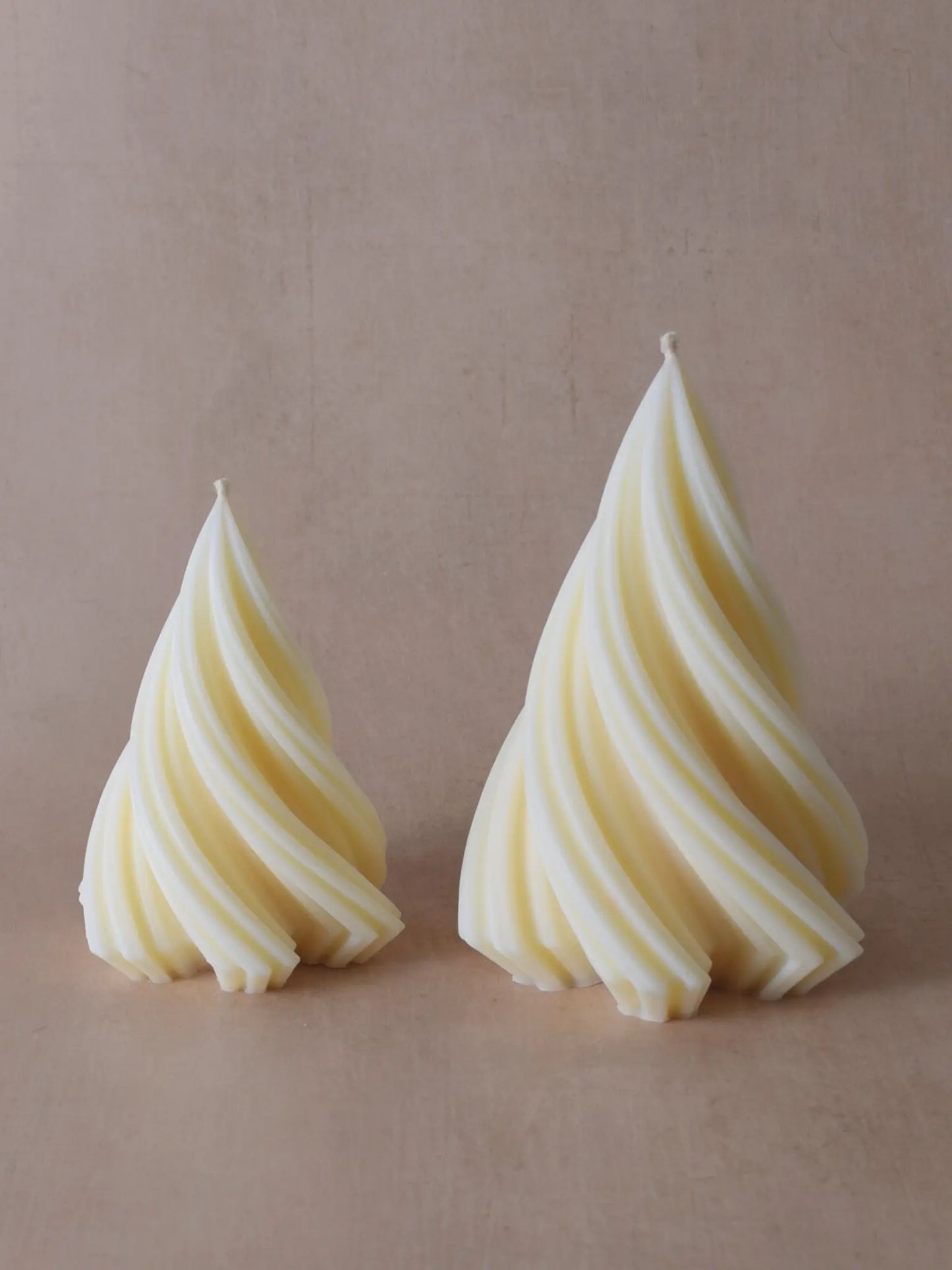 Kleine und grosse naturfarbene Kerzen in Weihnachtsbaumform vor einem beigen Hintergrund.