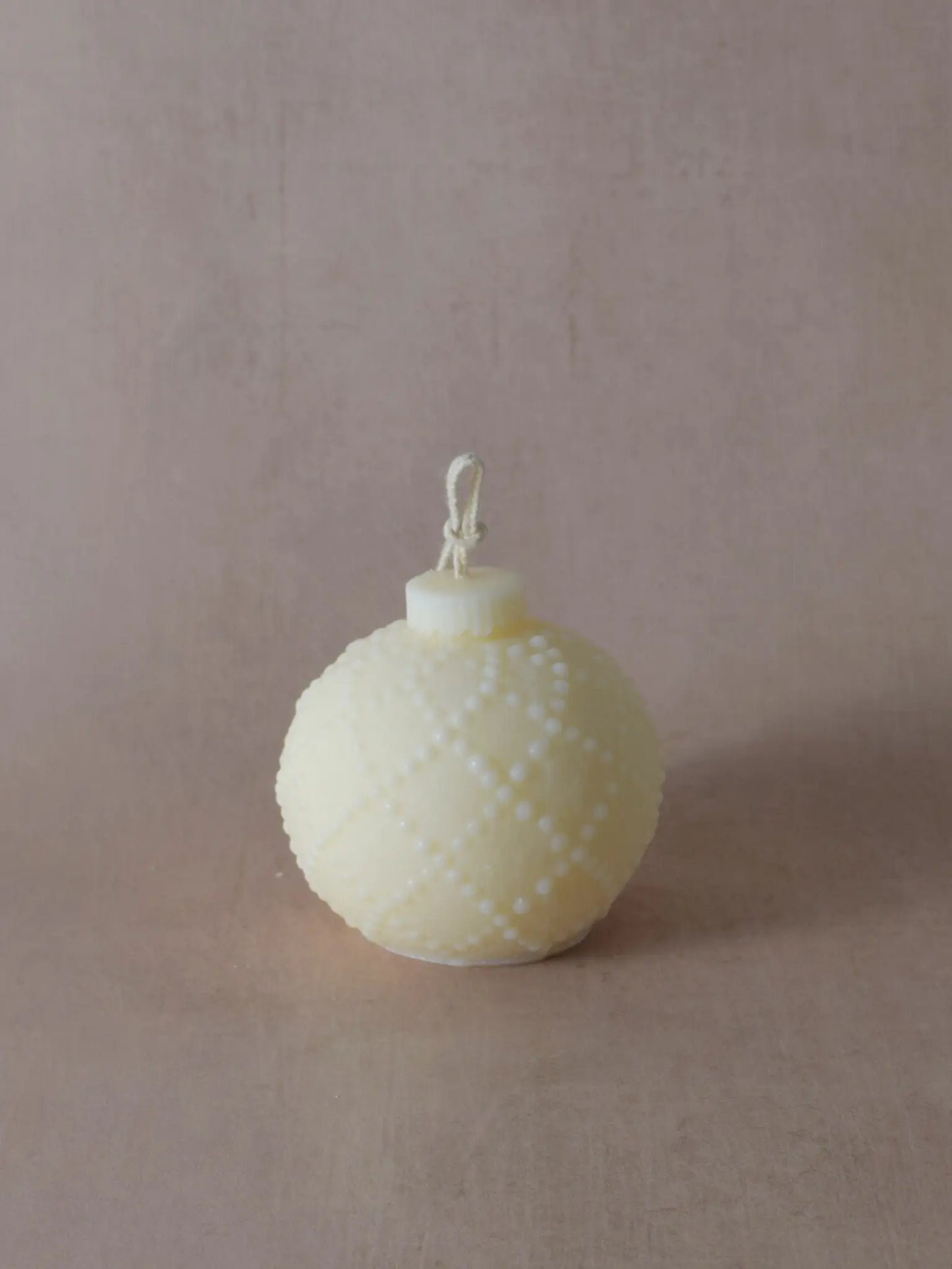 Naturfarbene Kerze in Weihnachtskugelform mit kleinen Tupfen.