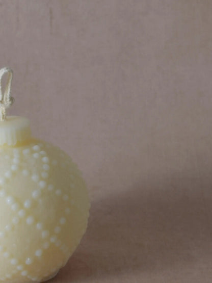 Nahaufnahme einer naturfarbenen Kerze in Weihnachtskugelform mit kleinen Tupfen.