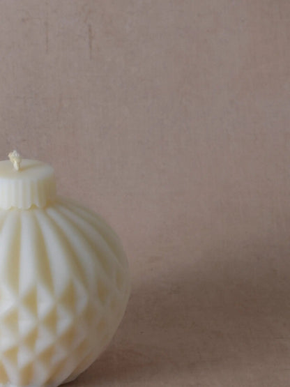 Nahaufnahme einer naturfarbenen Kerze in Weihnachtskugelform mit Streifen.