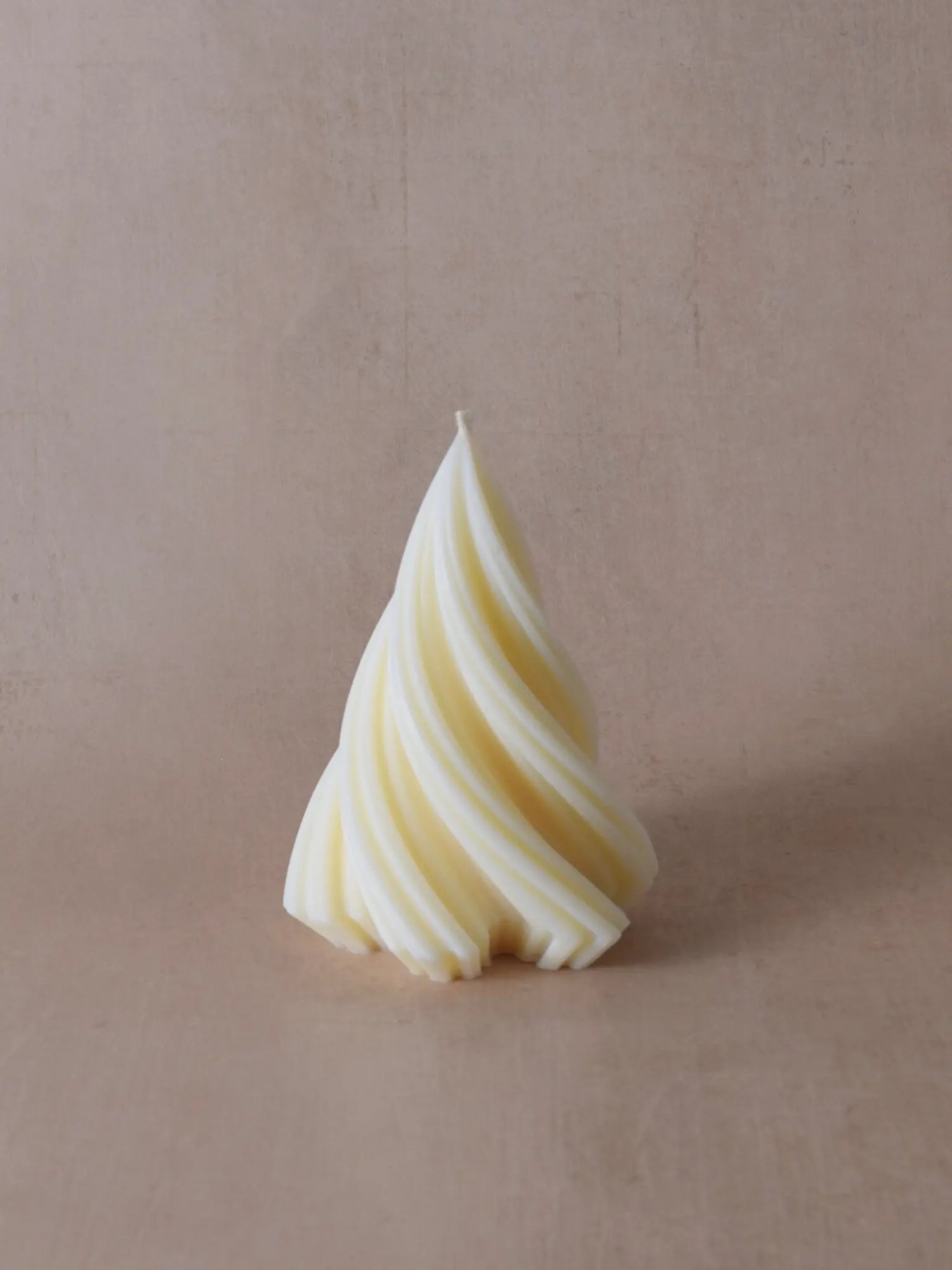 Kleine naturfarbene Kerze in Weihnachtsbaumform vor einem beigen Hintergrund.
