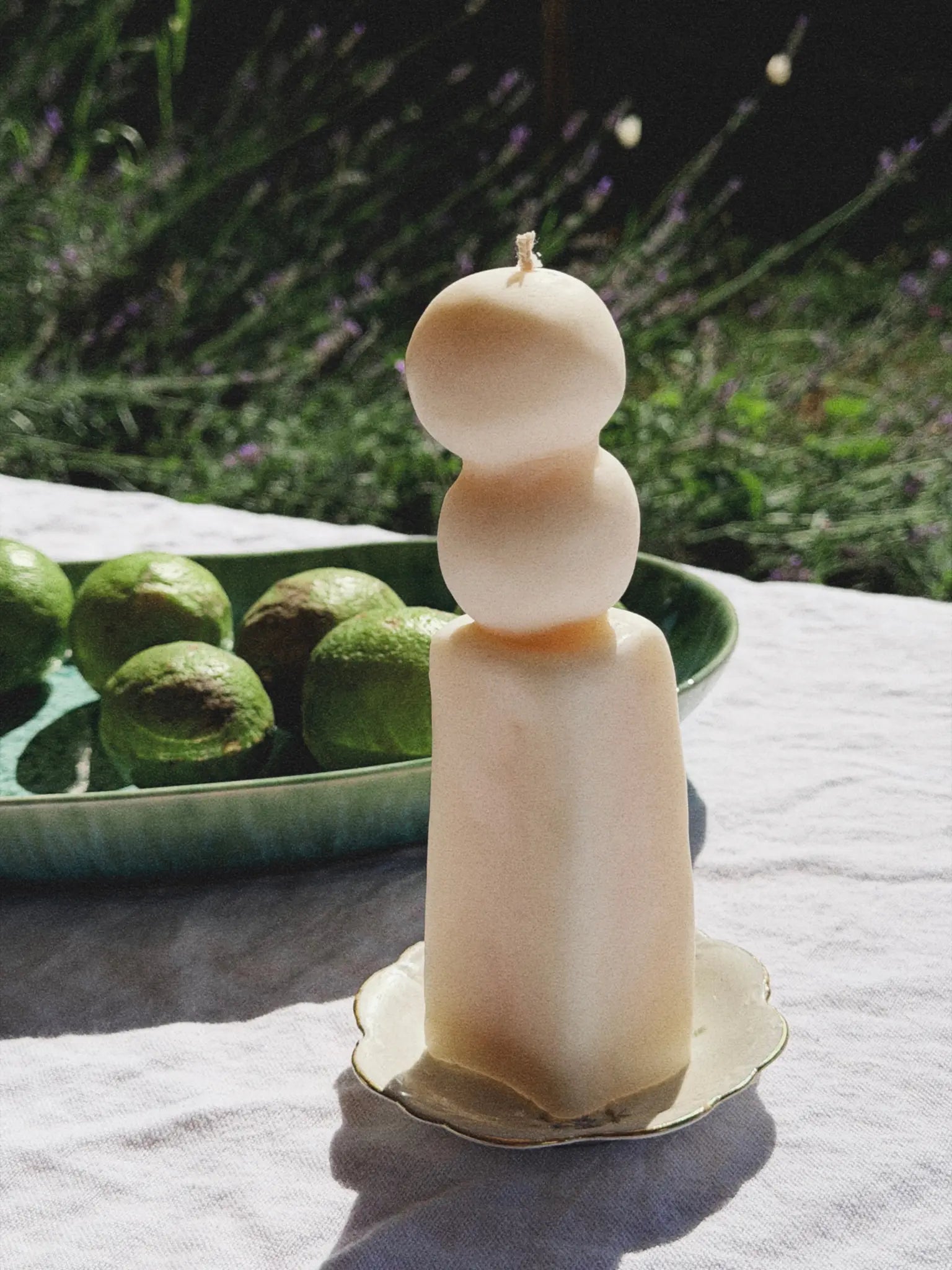 Dekokerze mit einem eckigen Unterteil und zwei aufeinander gestapelte Kugelnuf auf einem sommerlichen Tisch mit Limetten.