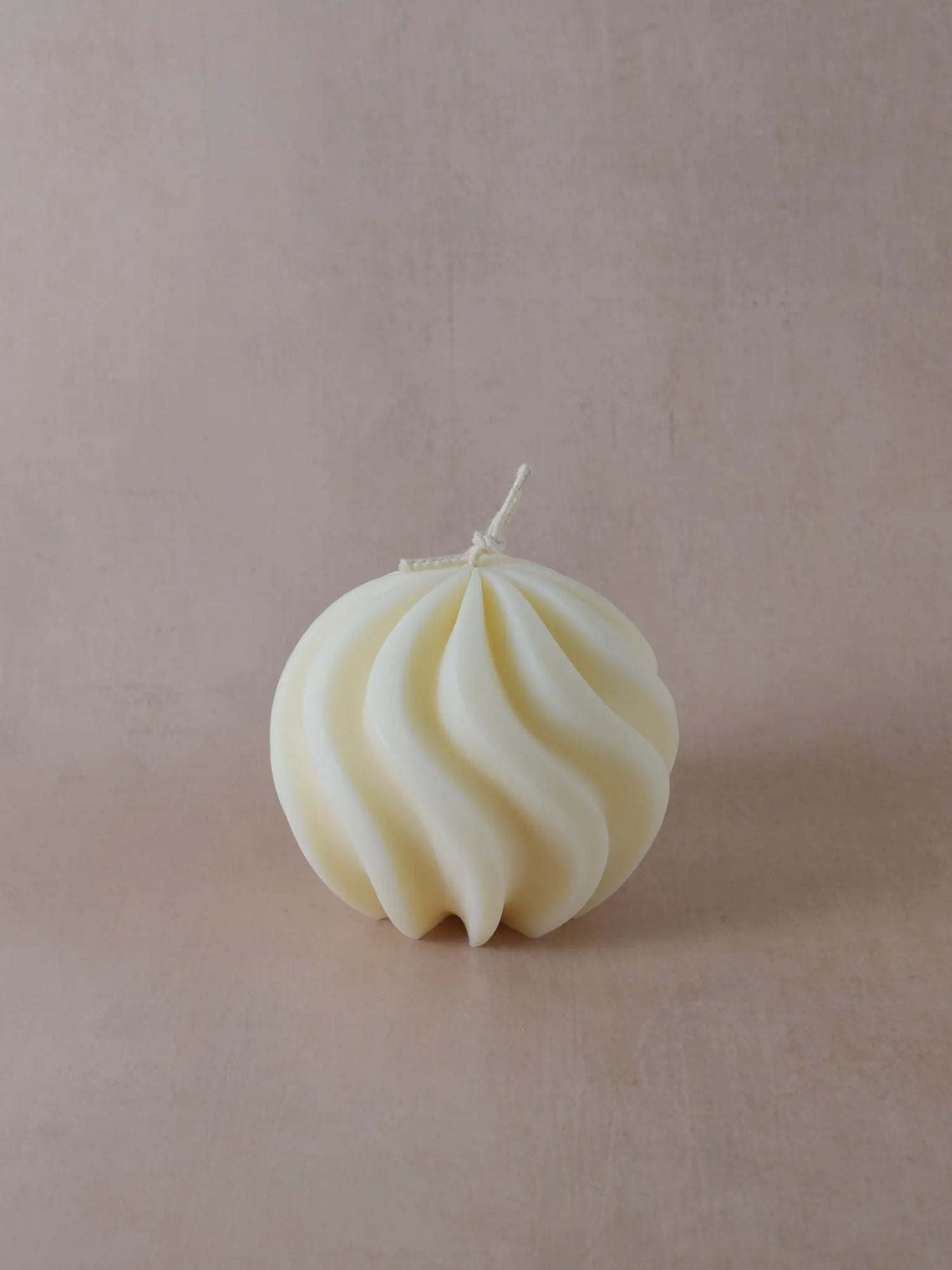 Runde Kerze mit geschwungenen Linien in naturweiss auf einem beigen Hintergrund