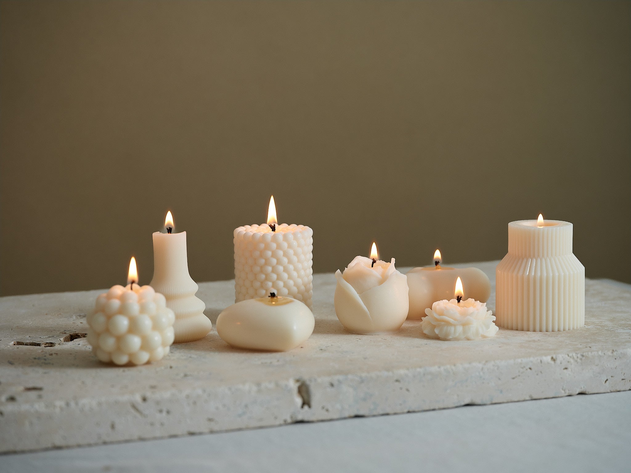 Unterschiedliche Dekokerzen in kunstvollen Designs auf Natursteinplatte