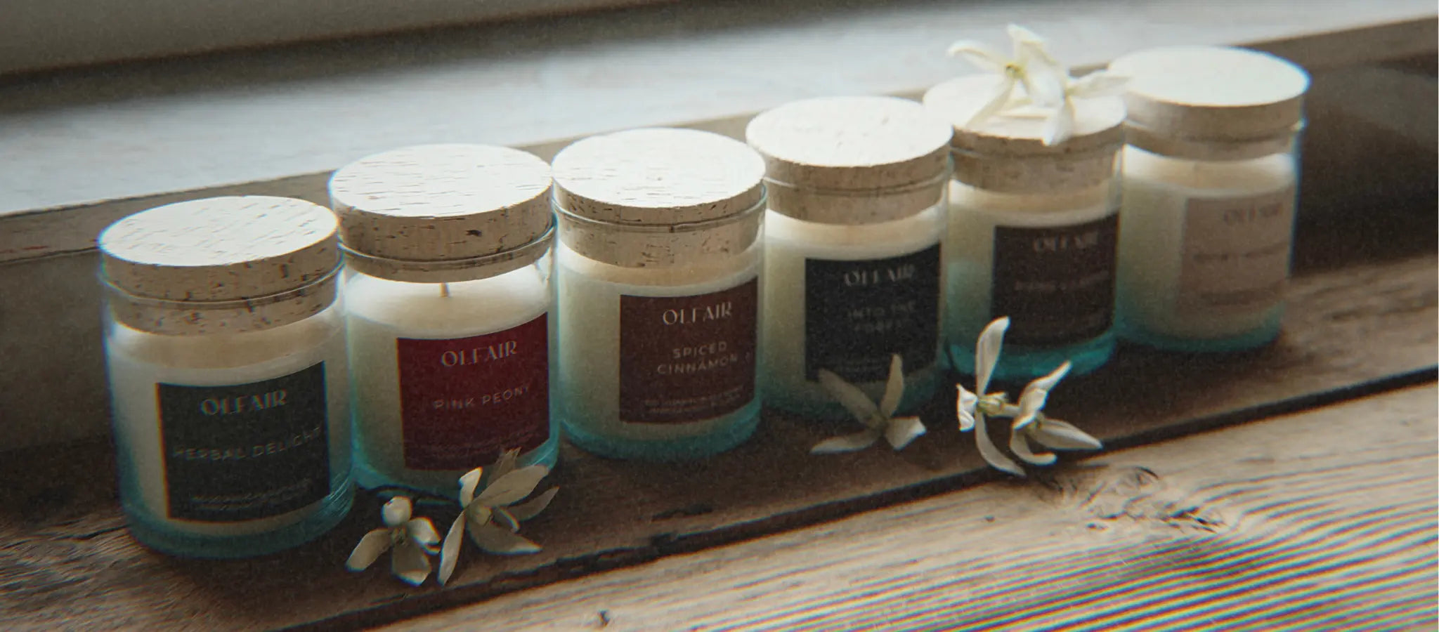 Sechs Duftkerzen in einer Reihe auf einem verwitterten Brett.