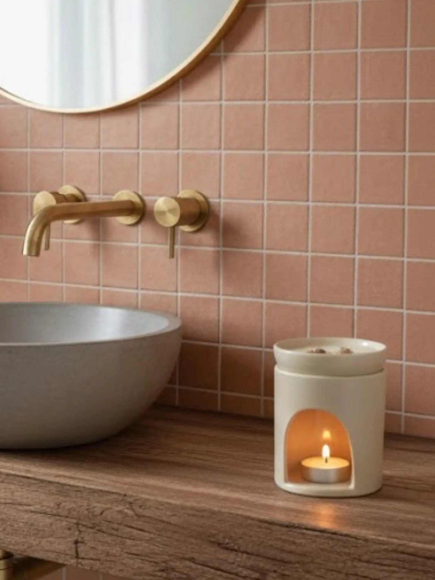 Weisse Duftlampe mit brennendem Teelicht in einem Badezimmer mit Terracotta Kacheln und einem Waschbecken aus Beton auf einem Holztisch.