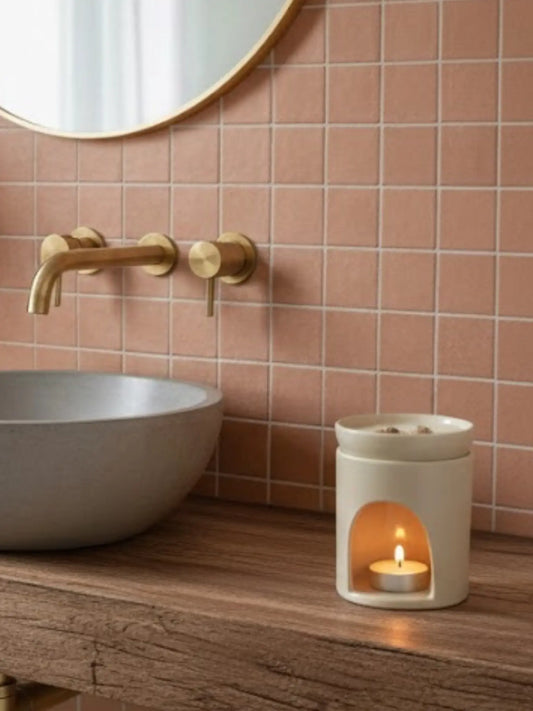 Weisse Duftlampe mit brennendem Teelicht in einem Badezimmer mit Terracotta Kacheln und einem Waschbecken aus Beton auf einem Holztisch.