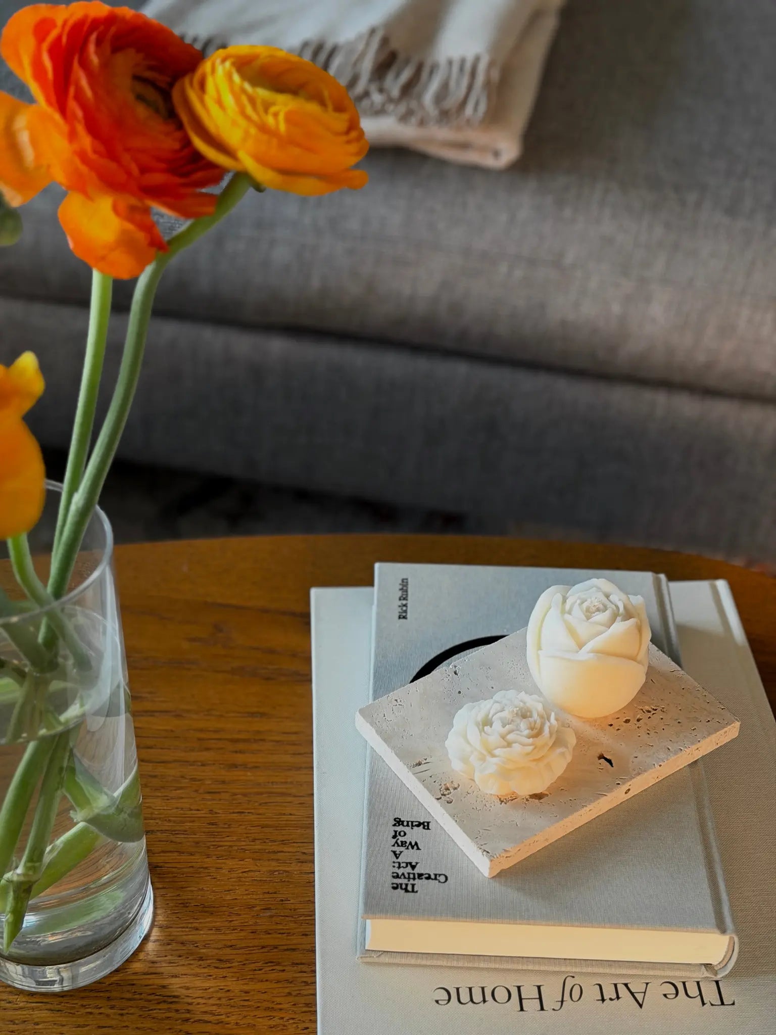 Eine Pfingstrosen und eine Rosen Kerze auf einem Couchtisch aus Holz. Die Kerzen stehen auf zwei Bücher daneben ist ein Blumenstrauss.