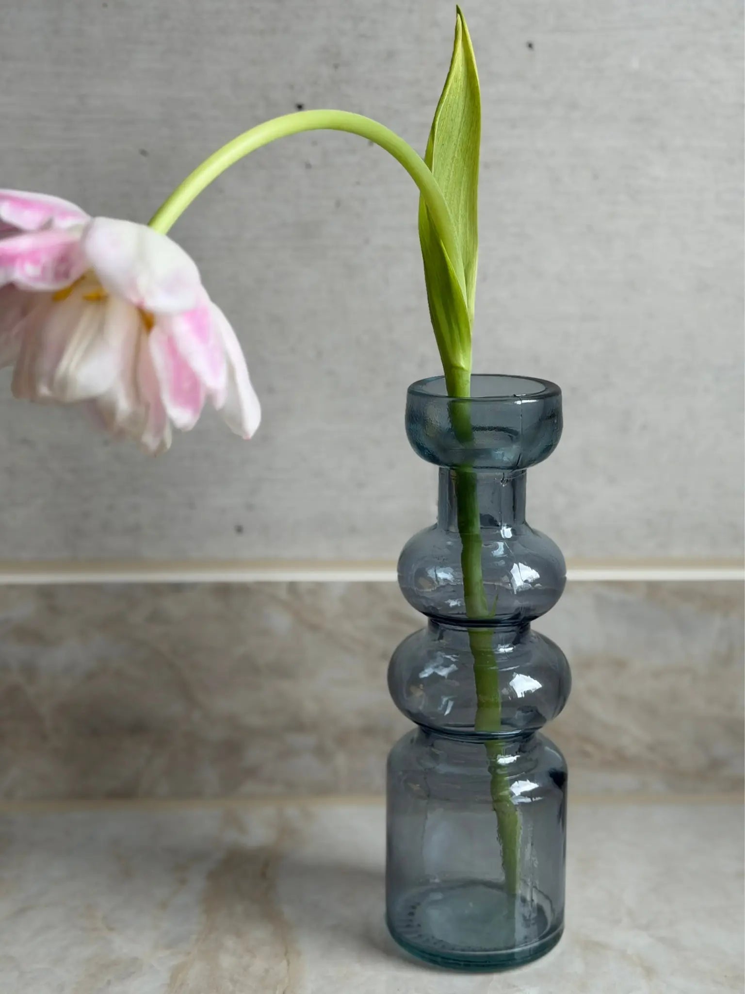 Blauer, gewölbter Kerzenhalter vor einem Marmor Hintergrund mit einer Blume