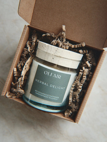 Geschenkbox mit Duftkerze Herbal Delight vor einem Marmor Hintergrund.