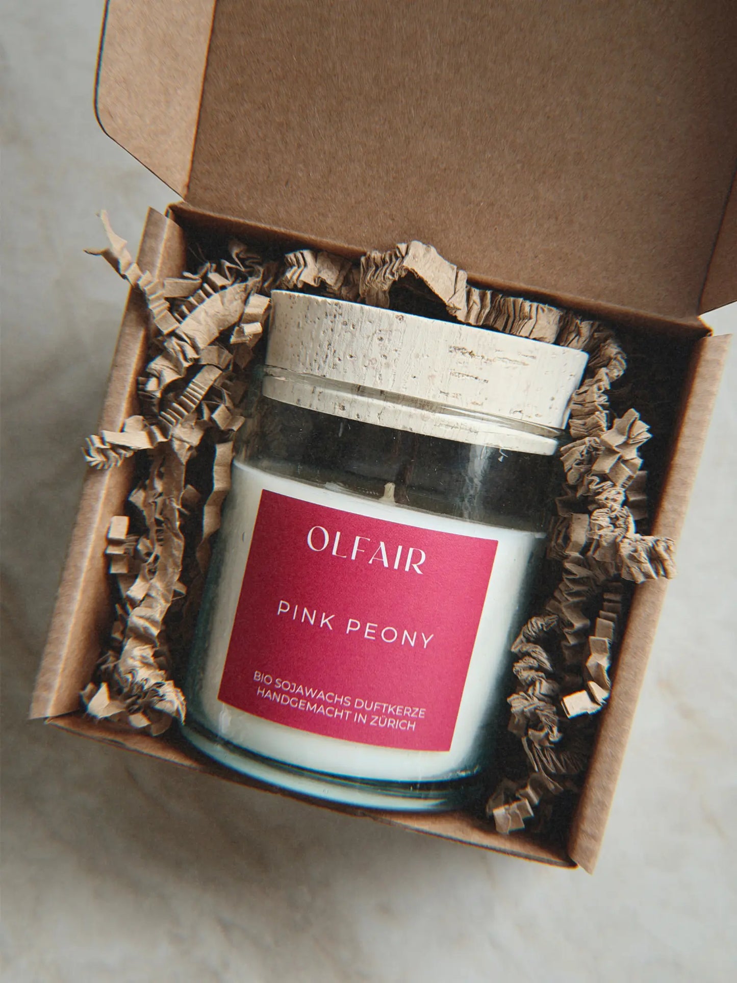Geschenkbox mit Duftkerze Pink Peony vor einem Marmor Hintergrund.