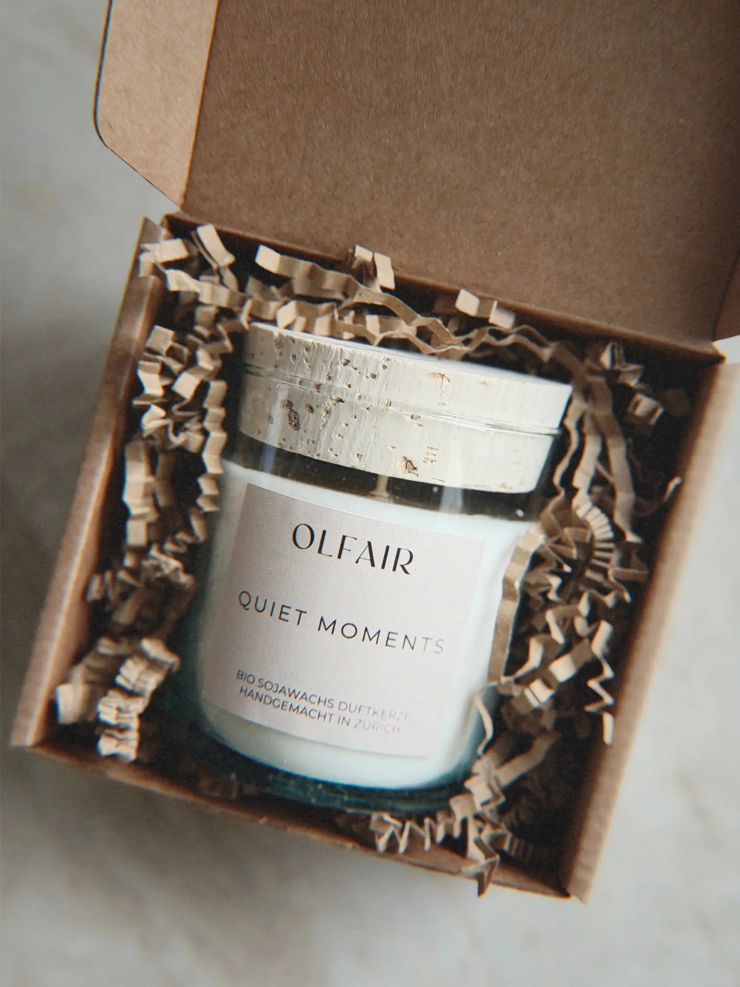 Geschenkbox mit Duftkerze Quiet Moments vor einem Marmor Hintergrund.