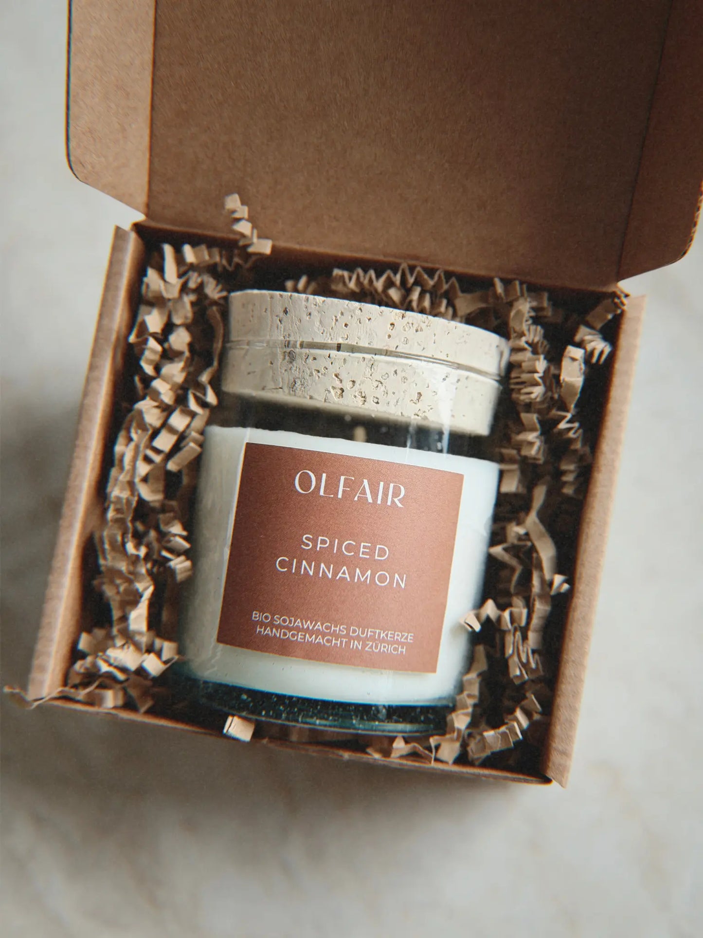 Geschenkbox mit Duftkerze Spiced Cinnamon vor einem Marmor Hintergrund.