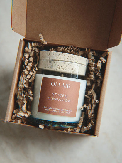 Geschenkbox mit Duftkerze Spiced Cinnamon vor einem Marmor Hintergrund.