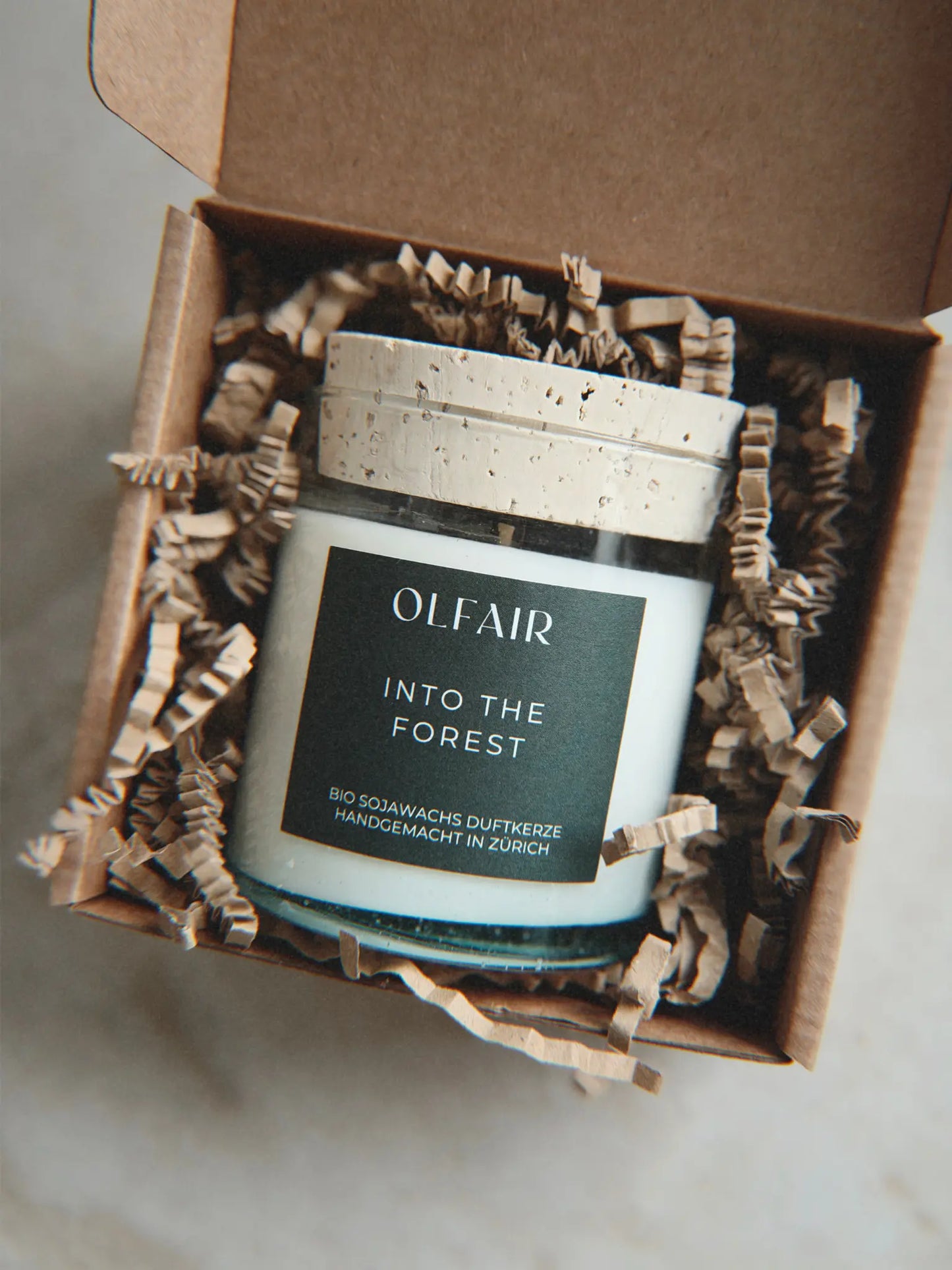 Geschenkbox mit Duftkerze Into the Forest vor einem Marmor Hintergrund.