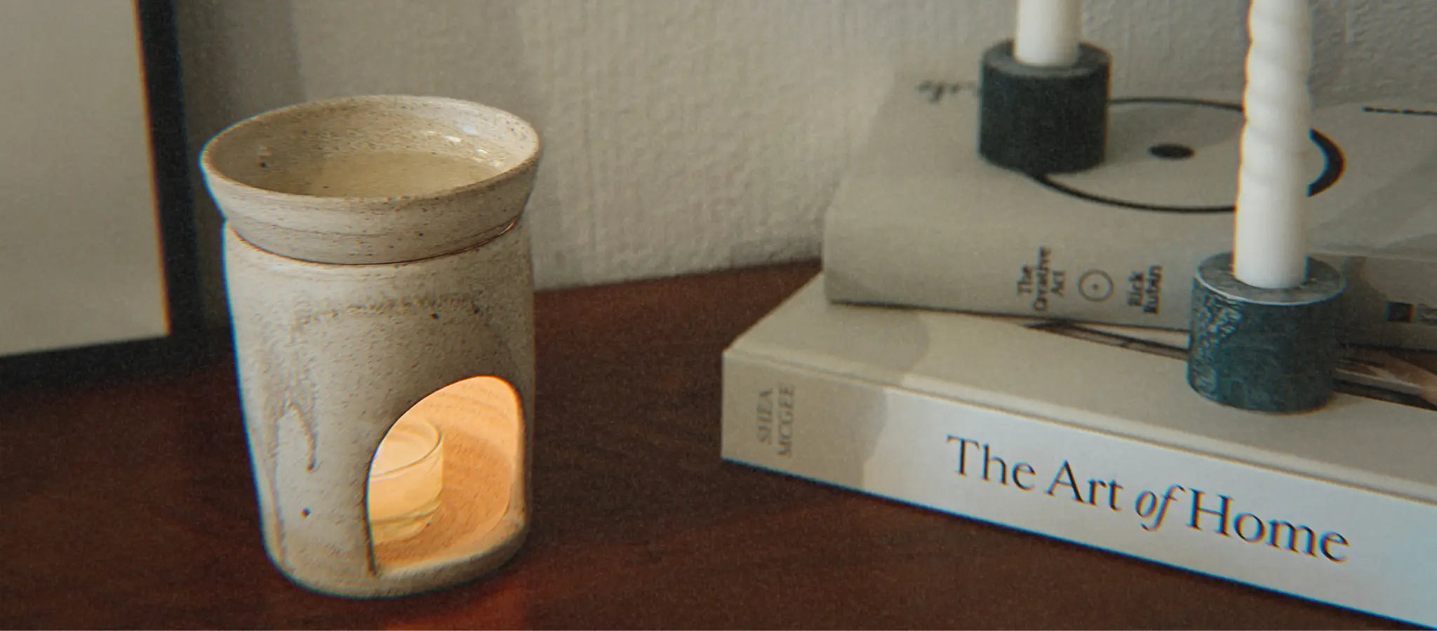 Geschmolzener Duftwachs in einer brennenden Duftlampe. Daneben stehen zwei gestapelte Bücher und weisse Stabkerzen.