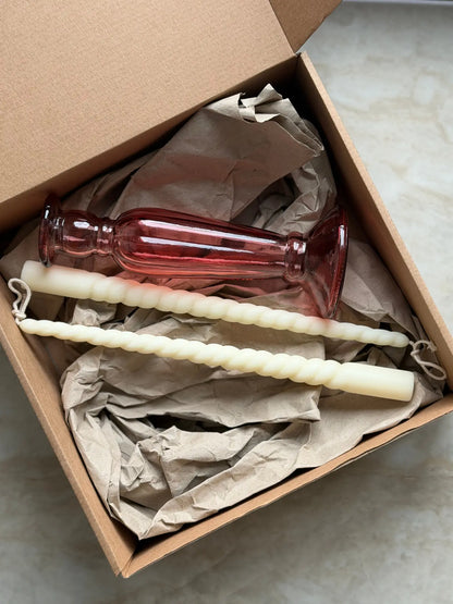 Geschenkset bestehend aus einem 2er-Set gedrehter Stabkerzen und einem rosafarbenen Kerzenhalter aus Recycling-Glas