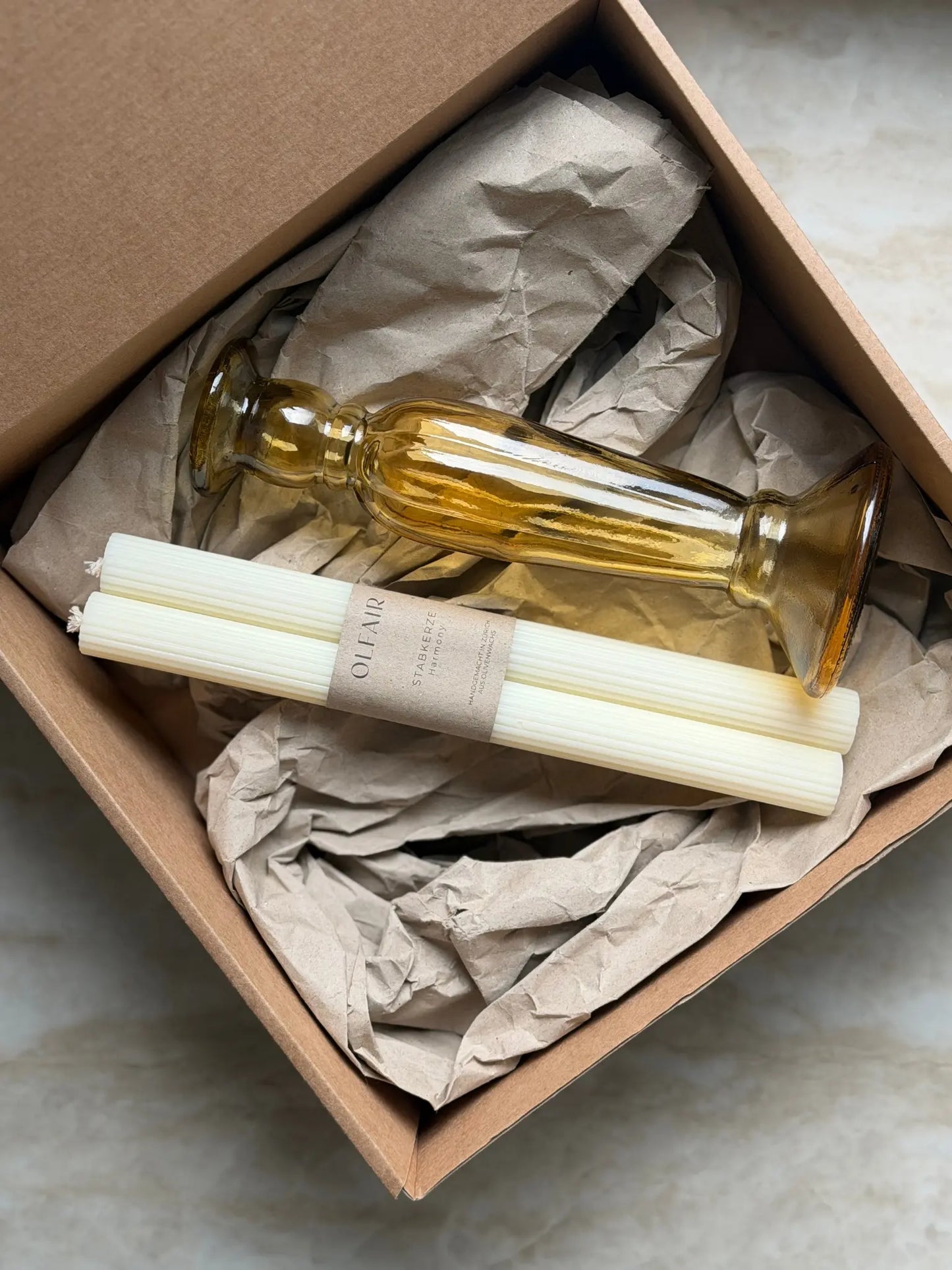 Geschenkset bestehend aus einem 2er-Set Stabkerzen mit kleinen Rilen und einem bernsteinfarbenen Kerzenhalter aus Recycling-Glas